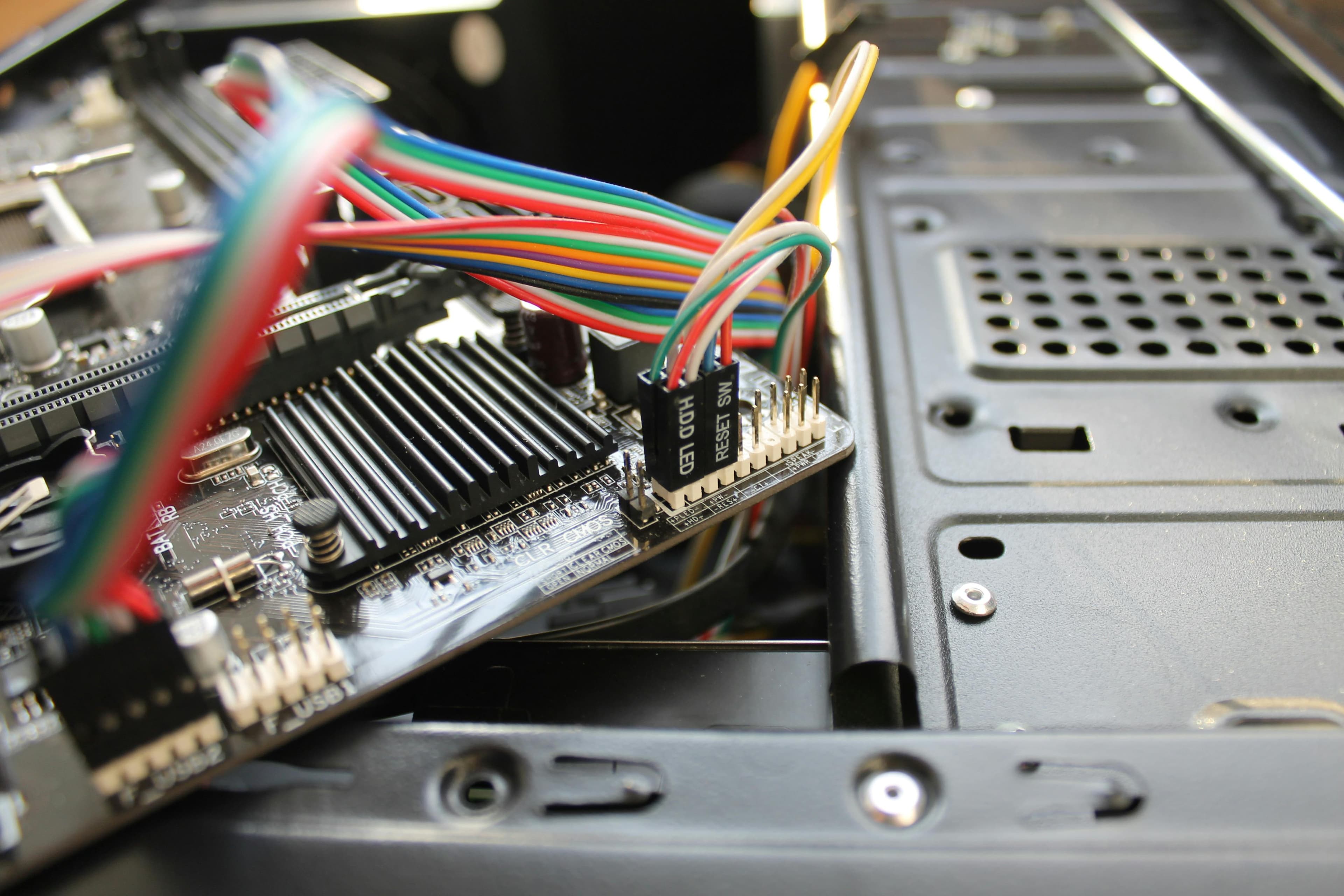 Blick in ein geöffnetes Computergehäuse mit Mainboard, an das bunte Kabel angeschlossen werden.